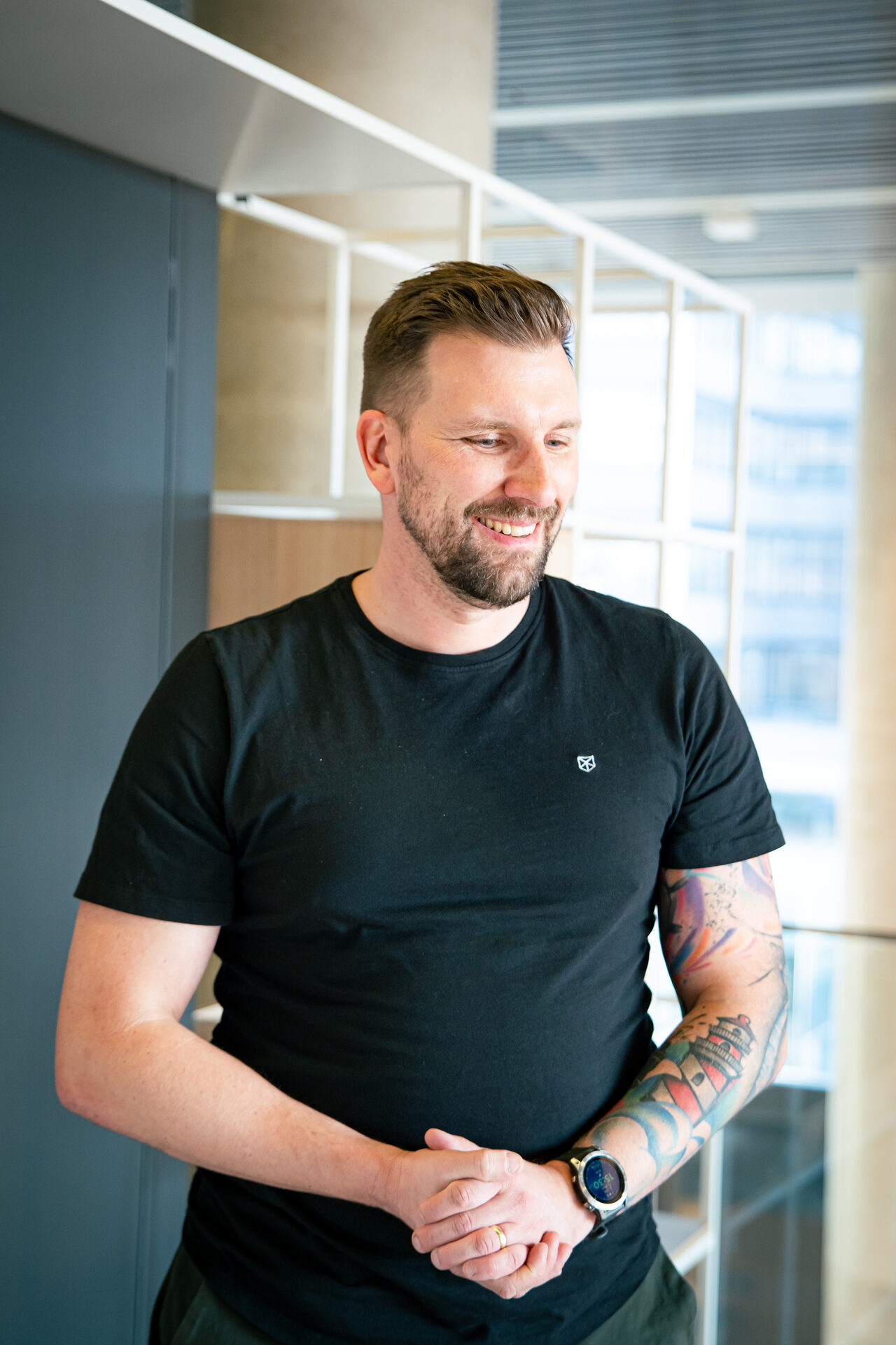 Jakub Lisner, Recruitment a Employer Branding Lead ve společnosti Vodafone, se usmívá v prosvětlených kancelářích ve Stodůlkách během natáčení série HR Vibecheck od agentury VERYGUD. Na sobě má černé triko s krátkým rukávem.