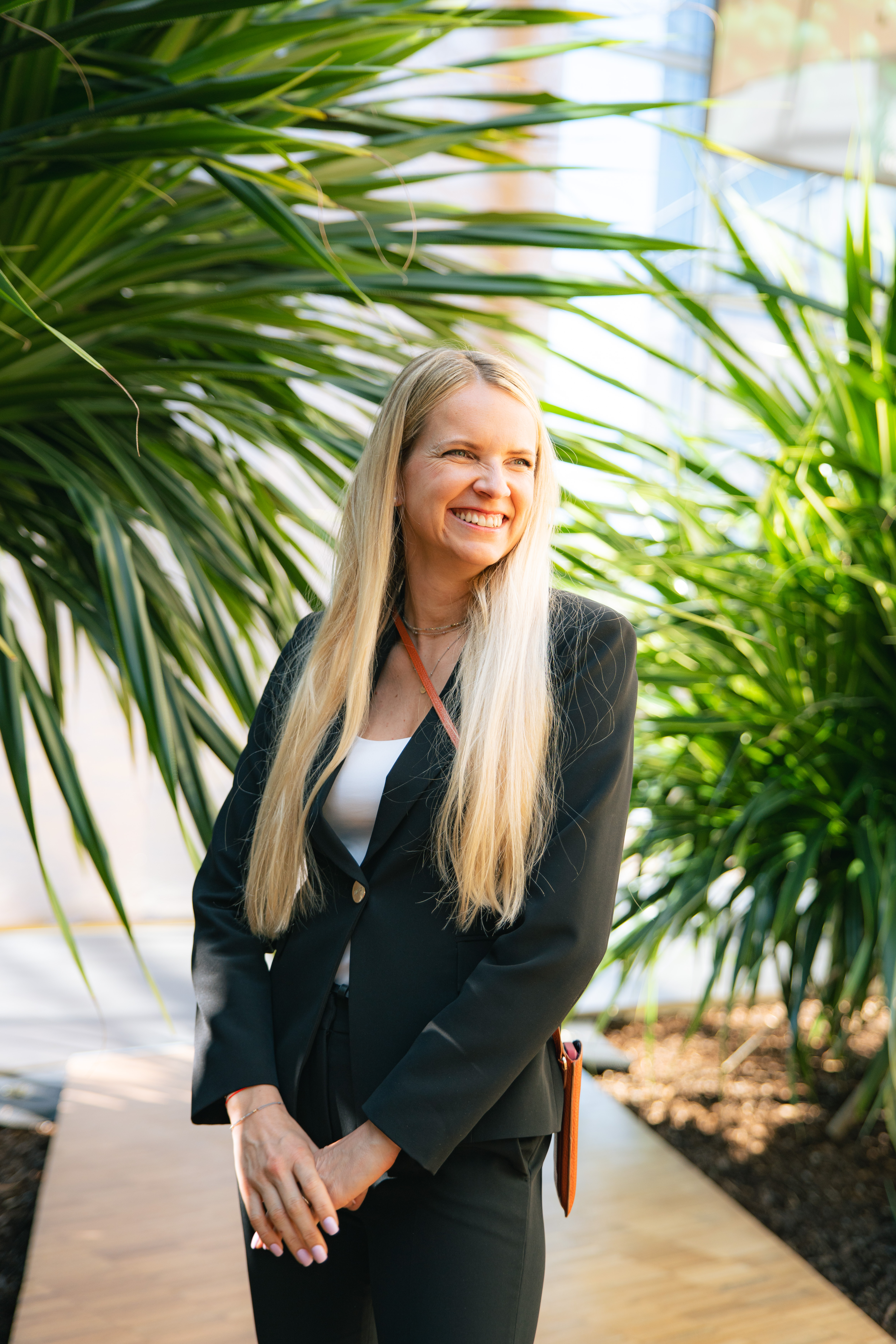 Zuzana Burianová, Head of HR z Nestlé, se široce usmívá a dívá se mimo objektiv fotoaparátu. Má rozpuštěné dlouhé blond vlasy, na sobě bílé triko a elegantní černé sako s knoflíky. Fotografie vznikla v prosvětleném interiéru officu Nestlé obklopeném velkými zelenými rostlinami během natáčení série HR Vibecheck od agentury VERYGUD.